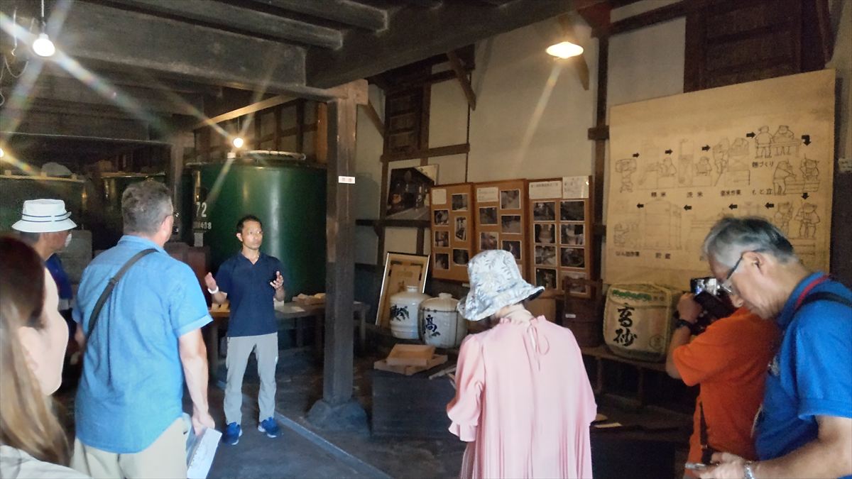 Takasago Brewery owner explaining the sake brewing process to visitors during an English-guided tour.